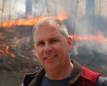 A headshot of Mike Wotton with a controlled burn going on in the background.